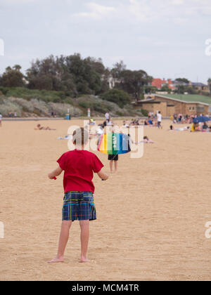 Deux petits garçons en premier plan un holding de contrôle à distance d'un autre cerf-volant multicolore et le lancement de cerf-volant tenant en l'air sur une plage magnifique. Banque D'Images