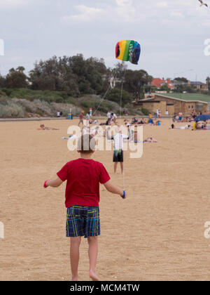 Deux petits garçons en premier plan un holding de contrôle à distance d'un autre cerf-volant multicolore et le lancement de cerf-volant tenant en l'air sur une plage magnifique. Banque D'Images