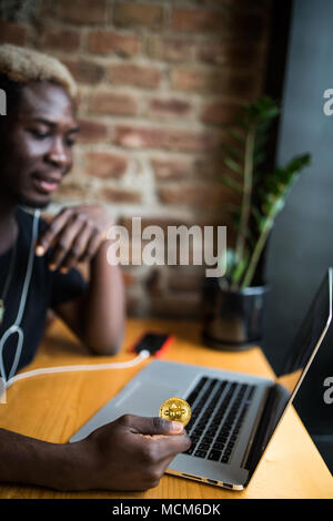 Homme jeune avec en main des bitcoins en face de laptop in cafe Banque D'Images