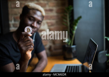 Homme jeune avec en main des bitcoins en face de l'ordinateur portable Banque D'Images