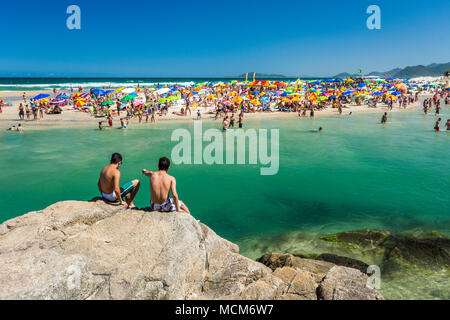 Deux jeunes gens assis sur un affleurement rocheux L'observation d'une scène de plage bondée à Ilha do Papagaio sur le rivage de l'État de Santa Catarina, Brésil Banque D'Images