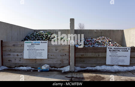 Les boîtes métalliques et les bouteilles en verre teinté vert et dans les bacs de collecte de recyclage communautaire avec des panneaux affichant des lignes directrices Banque D'Images