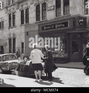 Années 1960, historique, Londres, un vendeur de fruits de la rue desservant une clientèle féminine. Derrière eux est une "Maison des Bewlay' store, un détaillant de tabac et des tuyaux d'abord établi à Londres en 1780 dans le Strand par Thomas Bewlay. A cette époque, il avait plus de 50 magasins à Londres et le même nombre situés dans des villes et dans le reste de la Grande-Bretagne. Fumer la pipe était une activité de loisirs populaire à cette époque. Banque D'Images