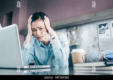 Souligné Asian businesswoman couvrir son visage avec la main et sentir la dépression sur un travail en face de votre ordinateur lors de l'établissement social,pression dans office Banque D'Images