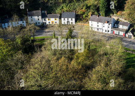 Regardant vers le bas sur les maisons et arbres éclairés par la lumière d'automne sur un coude de la route A6. Vue d'Tor, Matlock, Derbyshire, Angleterre, RU Banque D'Images