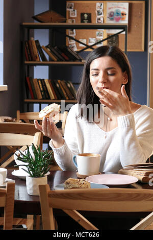 Fille dans un café avec une beigne et léchant ses doigts Banque D'Images