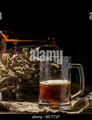 La bière mousseuse versée dans la tasse vide sur fond de bois Banque D'Images