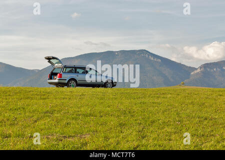 Voiture berline avec coffre ouvert sur le haut de la colline d'été. ciel bleu et les montagnes en arrière-plan. Banque D'Images