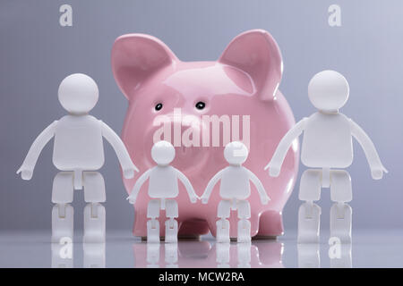 Famille de figures humaines standing in front of Pink Piggy Bank contre l'arrière-plan gris Banque D'Images