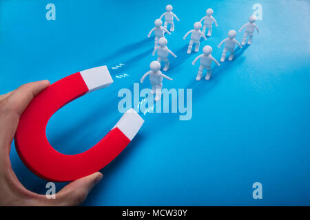 Close-up of a person's Hand Pulling figures humaines avec aimant fer à cheval sur fond bleu Banque D'Images