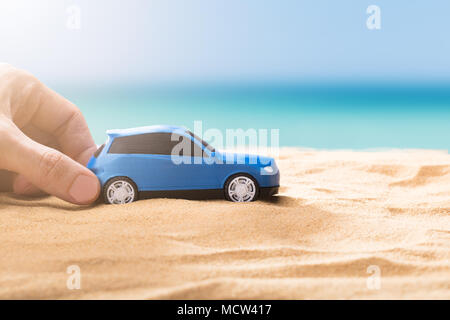 Human Hand Holding petite voiture bleue On Sandy Beach Banque D'Images