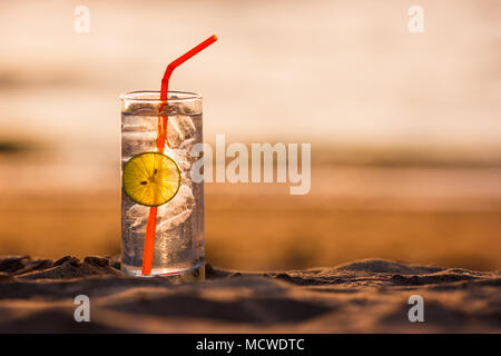 Photo d'un verre de Gin Tonic avec de la paille et chaux tranche sur la plage, au coucher du soleil. Long Beach, Ko Lanta, Thaïlande. Banque D'Images