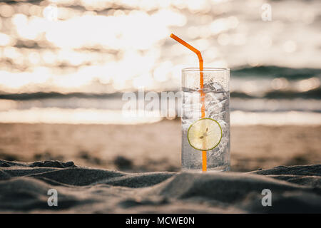 Photo d'un verre de Gin Tonic avec de la paille et chaux tranche sur la plage, au coucher du soleil. Long Beach, Ko Lanta, Thaïlande. Banque D'Images