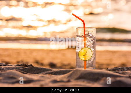 Photo d'un verre de Gin Tonic avec de la paille et chaux tranche sur la plage, au coucher du soleil. Long Beach, Ko Lanta, Thaïlande. Banque D'Images