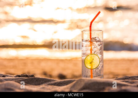 Photo d'un verre de Gin Tonic avec de la paille et chaux tranche sur la plage, au coucher du soleil. Long Beach, Ko Lanta, Thaïlande. Banque D'Images