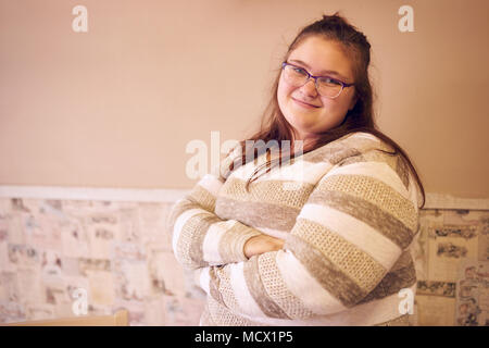 Portrait de belle chubby caucasian woman standing in front of a deux tons de mur à mur décoré de papier et les bras croisés en regardant la caméra et sourit. Banque D'Images