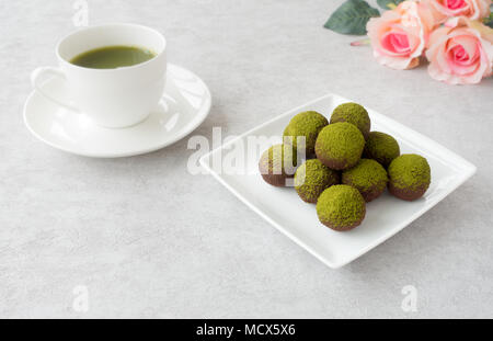 Matcha faits maison chocolats, une tasse de thé vert matcha et un bouquet de roses roses sur fond texturé gris clair. Banque D'Images