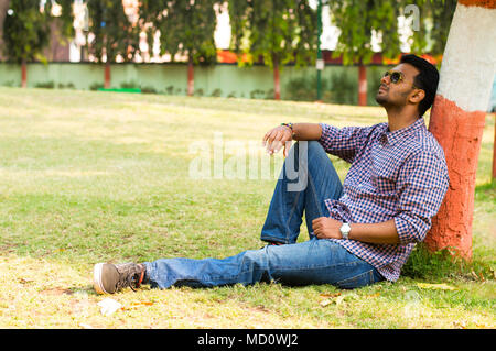 Jeune homme portant des lunettes de soleil et de détente leaning against tree Banque D'Images