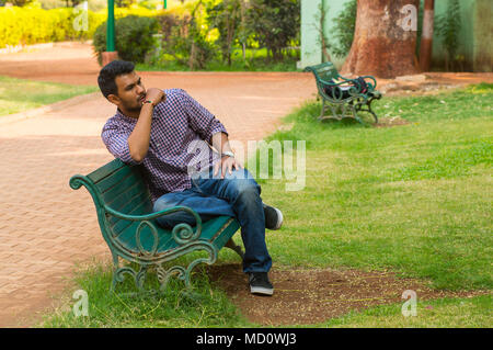 Guy looking away assis sur un banc dans un parc Banque D'Images