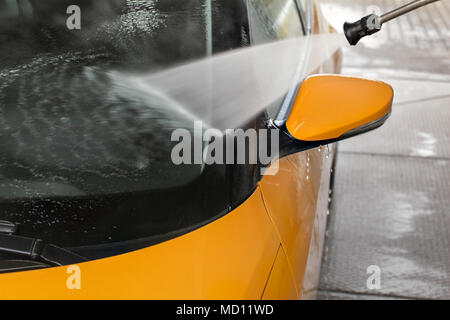 Détails sur jaune foncé vitre avant et arrière de voiture en miroir lavés avec jet d'eau pulvérisée dans carwash. Banque D'Images