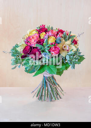 Beau bouquet de fleurs, roses multicolores avec des feuilles vertes se dresse sur une table gris clair, fond brun avec une arborescence Banque D'Images