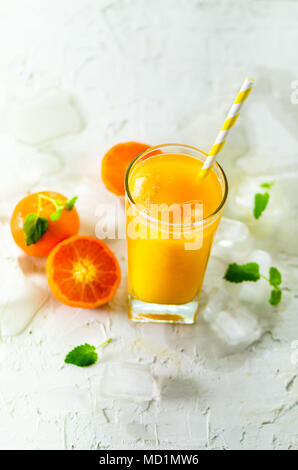 Jus de mandarine fraîche en verre sur fond blanc en béton. Fruits orange avec de la glace, menthe. Boissons froides pour chaude journée d'été. Copyspace. Banque D'Images