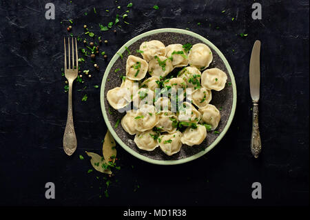 Préparé bouilli des pelmeni russes, boulettes, ravioli à la viande sur plaque gris avec du persil, poivre noir, fond en béton. Vue d'en haut. Banque D'Images