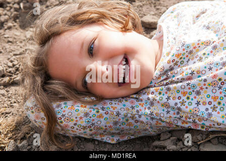 Jeune fille portant sur le sol et souriant pendant les jours ensoleillés. Banque D'Images