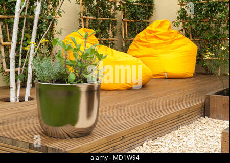 Close-up de plantes en pot et lumineuses, colorées de pouf jaune sur le bois des chaises de terrasse - 'Le Voyage Garden' - RHS Flower Show, Tatton Park, Angleterre, RU Banque D'Images