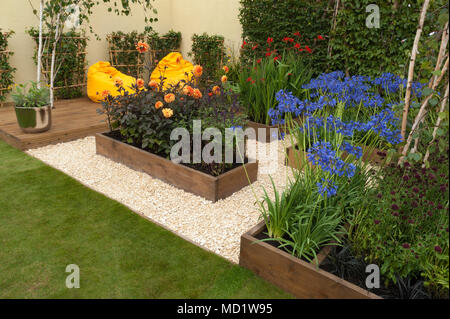 Plantes à fleurs de couleurs vives et de lits en bois et de chaises pouf jaune sur terrasse - jardin 'Le Voyage' - RHS Flower Show, Tatton Park, Angleterre, RU Banque D'Images