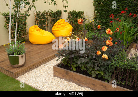 Plantes à fleurs de couleurs vives et de lits en bois et de chaises pouf jaune sur terrasse - jardin 'Le Voyage' - RHS Flower Show, Tatton Park, Angleterre, RU Banque D'Images