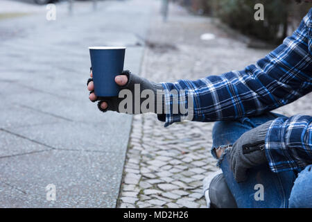 La main de mendiant portant des gants Holding Disposable Cup Banque D'Images