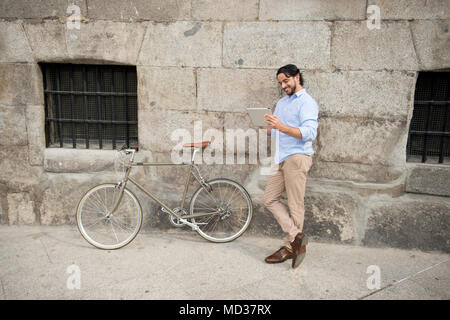 Young happy man attrayant dans les vêtements à la mode casual smiling happy en utilisant internet avec tablette numérique pavé numérique vintage rétro cool en vélo Banque D'Images