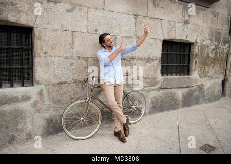 Young happy man attrayant dans les vêtements à la mode casual joyeux sourire à l'aide de téléphone mobile de prendre photo sur selfies vintage rétro cool en vélo Banque D'Images