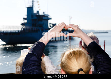 18 avril 2018, Kiel, Allemagne : une femme forme un coeur avec ses mains à Kiel's marine port pour le départ de l'appel d'offres «mosel'. Le navire appareille pour la mer Méditerranée où il a remplacé le 'Sachsen' frégate dans l'UE l'opération EUNAVFOR déploiement MED 'Sophia'. Photo : Frank Molter/dpa Banque D'Images