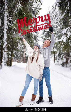 Jeune couple avec Joyeux Noël mots dans la neige Banque D'Images