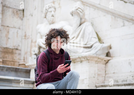 Beau jeune homme avec les cheveux bouclés tracksuit en utilisant son téléphone mobile en face de Dieu du Nil statue à Rome Banque D'Images