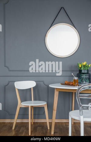 Un miroir rond avec cadre sur un mur gris avec au-dessus d'un petit moulage en bois, blanc, ensemble salle à manger dans un intérieur design Banque D'Images