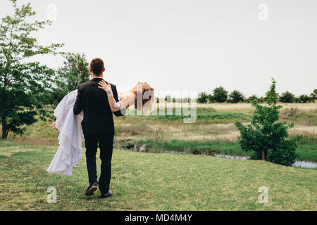 Vue arrière de l'époux avec son épouse et de s'éloigner dans le parc. Newlywed couple célébrant le mariage en plein air. Banque D'Images