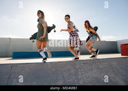 Groupe de femmes bénéficiant d'amis au skate park. Les jeunes femmes gaies tournant sur la rampe de planche à roulettes au skate park. Banque D'Images