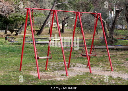 L'équipement de plein air de jeu public metal swing avec l'hiver arbres sans feuilles, d'autres l'équipement de terrain et de l'herbe non coupée en arrière-plan Banque D'Images