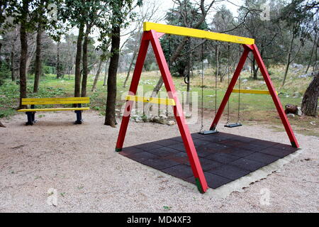 L'équipement de jeu public extérieur en forme de vintage en bois à swing avec banc en arrière-plan, entouré avec protection en caoutchouc, aire de jeux Banque D'Images