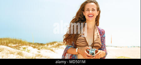 Ambiance bohème. vacances style tzigane smiling young woman in bikini sur la plage avec retro photo caméra Banque D'Images