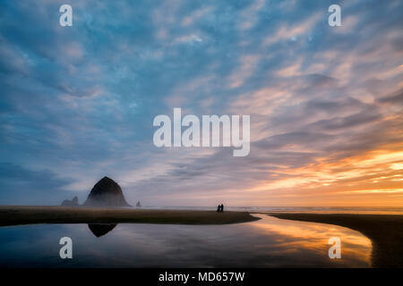 Cannon Beach au coucher du soleil avec Haystack Rock, flux et couple avec chien. Oregon Banque D'Images