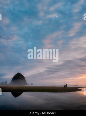 Cannon Beach au coucher du soleil avec Haystack Rock, flux et couple avec chien. Oregon Banque D'Images