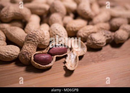 Pile de cacahuètes dans le naturel de l'unshelled shell sur un fond de bois naturel. Une arachide est ouvert dans le premier plan avec les écrous visibles à l'intérieur. Banque D'Images