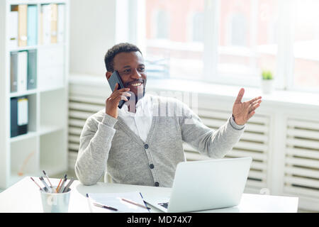 Smiling African American entrepreneur assis à un bureau et la conduite de négociations avec téléphone partenaire d'affaires, portrait Banque D'Images