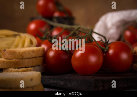 Photo horizontale avec twig plein de tomates cerises rouges placés sur planche de bois usé avec des tagliatelles et quelques morceaux d'ail bruschettas sonne. À côté de Banque D'Images