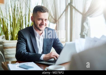 Jeune homme de race blanche manager working on laptop, l'écoute de sa collègue et souriant alors qu'il attendait pour le déjeuner dans le café Banque D'Images