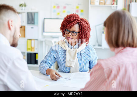African American female manager élégant rouge avec des cheveux bouclés avoir réunion d'affaires avec des collègues de bureau Banque D'Images